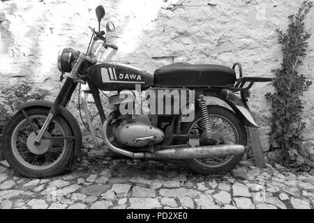 Black & white (monochrome) shot of classic vintage Czech Jawa motorbike parked on cobblestone street against a white wall in Albania Stock Photo