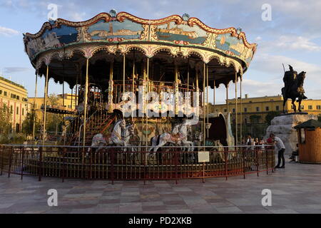 Children riding old fashioned carousel in Skanderbeg Square, Tirana, capital of Albania with monument of national hero Sheshi Skënderbej on the right Stock Photo