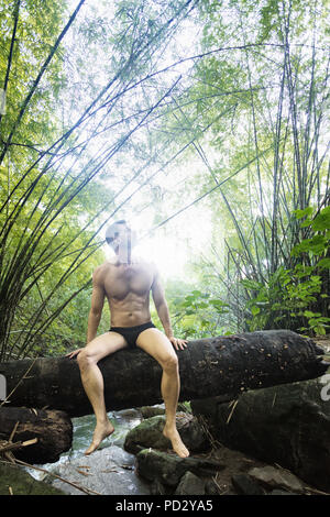 Man on tree trunk over stream in rainforest, Guaiuba, Ceara, Brazil Stock Photo