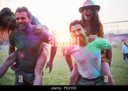 Two young couples covered in coloured chalk powder piggybacking at Holi Festival Stock Photo