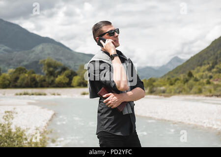 Businessman on mountain riverside making smartphone call, Francenigo, Veneto, Italy Stock Photo