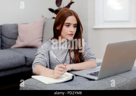 Woman writing notes into notepad from laptop Stock Photo