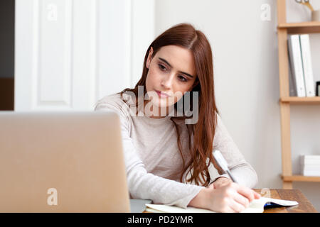 Woman writing notes into notepad from laptop Stock Photo