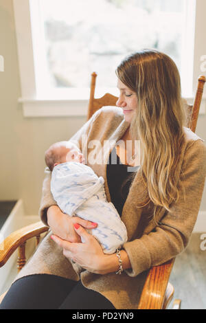 Mother sitting in rocking chair holding newborn baby boy Stock Photo