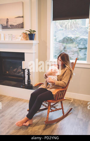 Mother sitting in rocking chair holding newborn baby boy Stock Photo