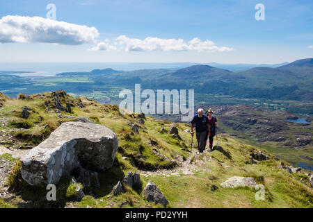 Two hikers hiking on path near Cnicht mountain top in Snowdonia National Park with scenic view to coast in summer.  Croesor Gwynedd Wales UK Britain Stock Photo