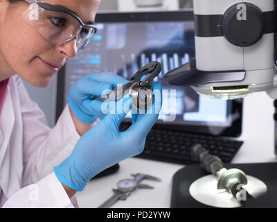 Engineer measures manufactured component for accuracy and quality control using dial caliper, 3D stereo microscope in background Stock Photo