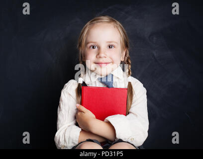 Cute little girl with book. Happy Child on empty blackboard background with copy space Stock Photo