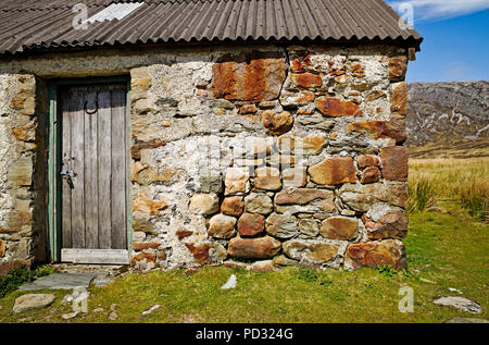Old weathered wooden door and stone wall of traditional stone hut with corrugated iron roof in remote moorland location in Sutherland, Scotland UK. Stock Photo