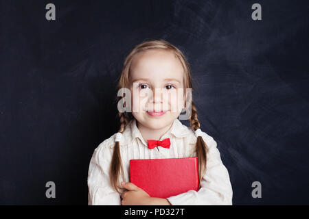 Smiling girl with red book on empty chalkboard background with copy space. Child portrait Stock Photo