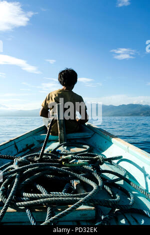 Gilli Trewangan, Indonesia. A young Indonesian man sits on the bow of a small boat carrying tourists between Gilli Trewangan and the island of Lombok. Stock Photo