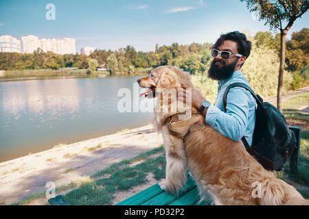 Young man sitting with his dog on the chair in the park, enjoyin Stock Photo