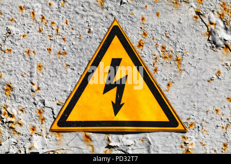 Yellow high voltage triangle warning sign on rusty gray metal wall, close-up photo Stock Photo