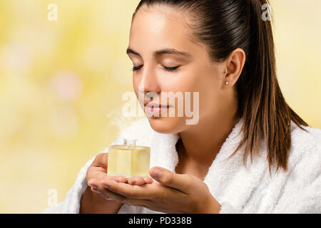 Close up portrait of woman in white spa gown smelling essential oil fragrance.Girl holding little bottle with aromatic scent. Stock Photo