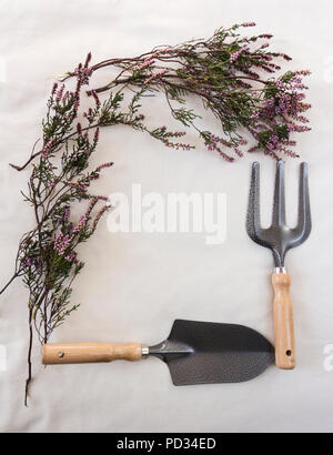 Purple autumn heather (erica) frame with garden tools set - hand fork and hand trowel on ecru piece raw cotton fabric. Stock Photo