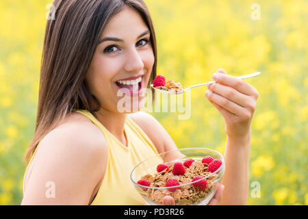 Close up face shot of attractive young woman eating healthy crispy whole grain cereal breakfast outdoors. Stock Photo