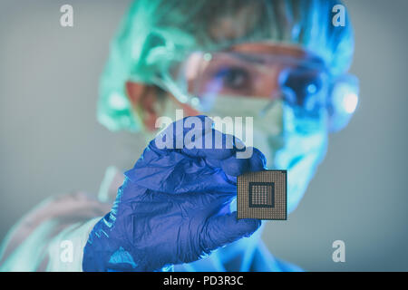 An engineer working in a laboratory wearing a special uniform and protective gloves holds new processor in hands and examines it Stock Photo