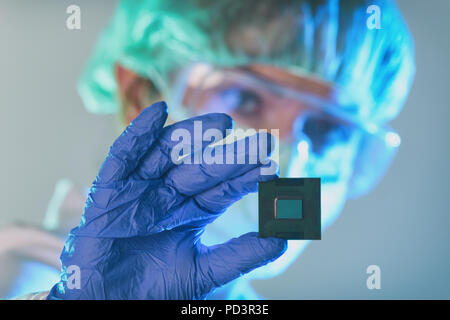 An engineer working in a laboratory wearing a special uniform and protective gloves holds new processor in hands and examines it Stock Photo