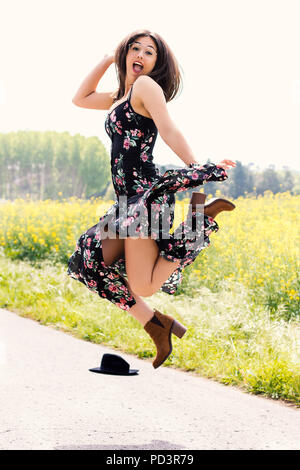 Full length action portrait of young girl in flower dress jumping outdoors. Stock Photo