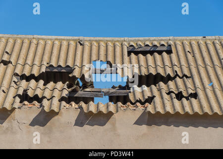 Corrugated asbestos roof in poor state of repair against a clear blue sky. Stock Photo