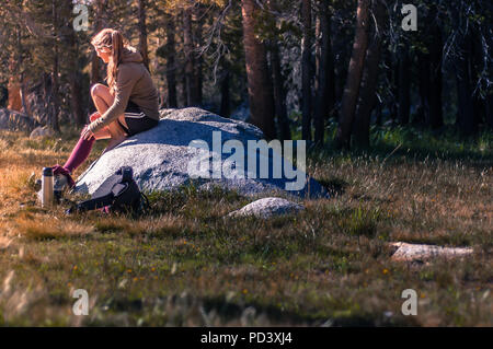 Young female hiker sitting on rock taking a break in Tuolumne Meadows, upper part of the Yosemite National Park, California, USA Stock Photo