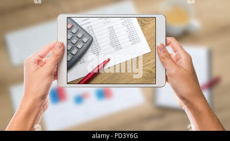 Business calculator and chart paper on white tablet screen with hands holding the device and office chart table in the background Stock Photo