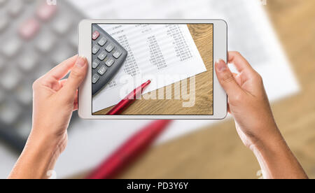 Business calculator and chart paper on white tablet screen with hands holding the device and office chart table in the background Stock Photo