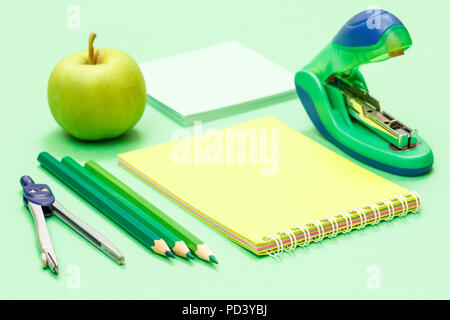 Compass, color pencils, notebook, apple, note paper and stapler on green background. Back to school concept. School supplies Stock Photo