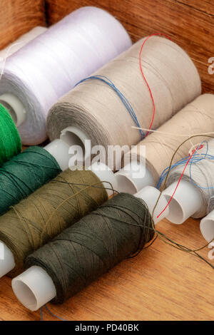 A closeup photo of sewing thread spools, beige and brown, in a wooden box Stock Photo