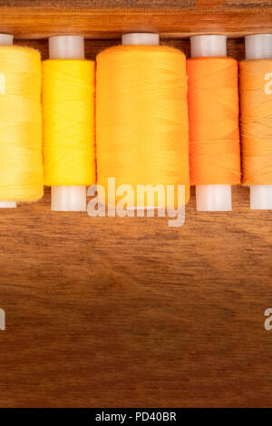 An overhead closeup photo of vibrant yellow and orange sewing thread spools in a wooden box Stock Photo