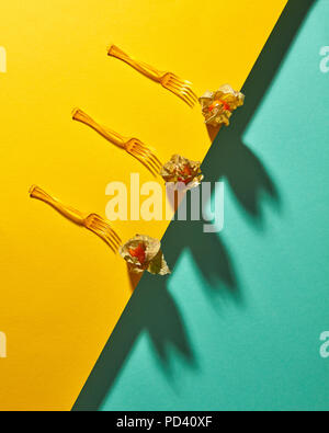 Flat lay view of the pattern of three yellow physalis fruit and forks with shadows on diagonally duotone yellow green background Stock Photo