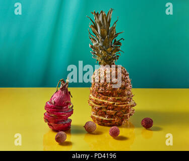 Tropical Pineapple fruit single whole and dragon fruit, pitaya made up of sliceson and litchi fruits on a duotone yellow-blue background Stock Photo