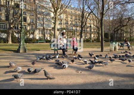 Mother and daughters feeding pigeons at a park near the Eiffel Tower in Paris Stock Photo