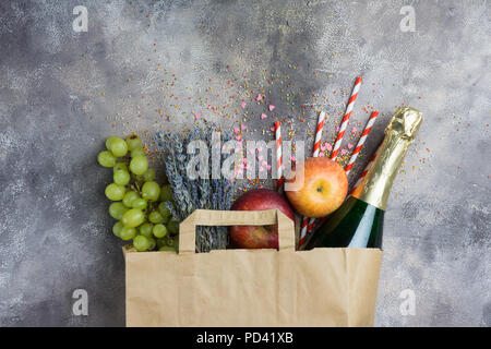Wine, fruits, flowers (set for the party or picnic) in a paper craft pack on a gray concrete background. Top view. Stock Photo