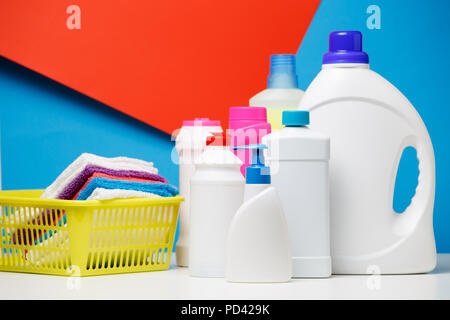 Photo of bottles of cleaning products and multi-colored towels in yellow basket isolated on red,blue background Stock Photo