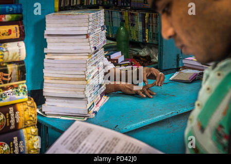 A man stretches his fingers while another reads at an open-air book store on College Street, Kolkata, India Stock Photo
