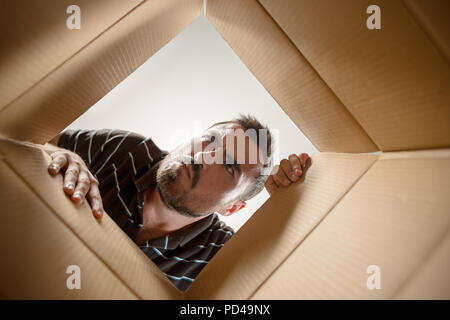 The surprised man unpacking, opening carton box and looking inside. The package, delivery, surprise, gift lifestyle concept. Human emotions and facial expressions concepts Stock Photo