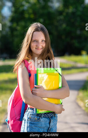 Little girl teenager. In the summer in city. In his hands he holds folders and notebooks. Emotionally smiling happily. Concept back to school. Stock Photo