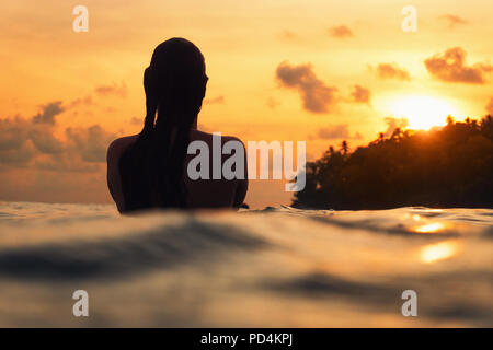 young woman from behind in indian ocean during orange sunset with romantic mood Stock Photo