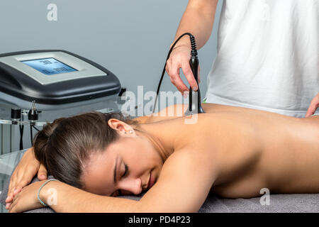 Close up of young woman receiving interferential electrotherapy.Therapist stimulating nerve on spine with apparatus. Stock Photo