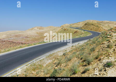 Curved asphalt road leading through the desert up a mountain, blue sky with text space Stock Photo