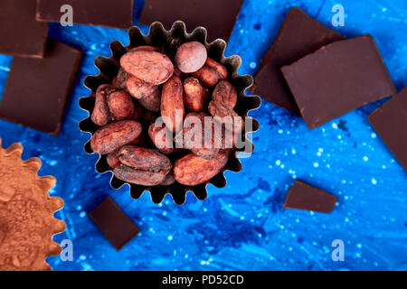 Cocoa beans background on blue table. Dark chocolate pieces and crushed cocoa powder carob. Top view. Copy space. Stock Photo
