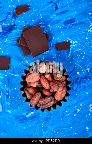 Cocoa beans background on blue table. Dark chocolate pieces and crushed cocoa powder carob. Top view. Copy space. Stock Photo