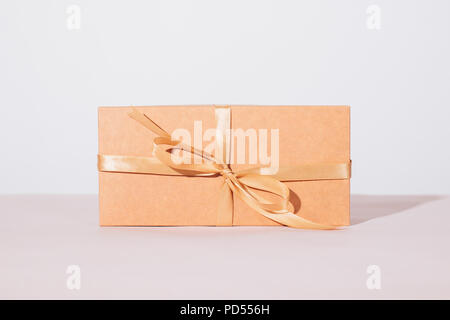 Brown cardboard gift box with beige satin ribbon on table on a white background, close-up. Stock Photo