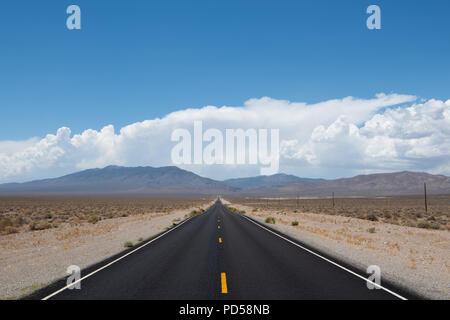 Desert highway vanishing into perspective into a mountain range under dramatic blue sky and white clouds in western Nevada