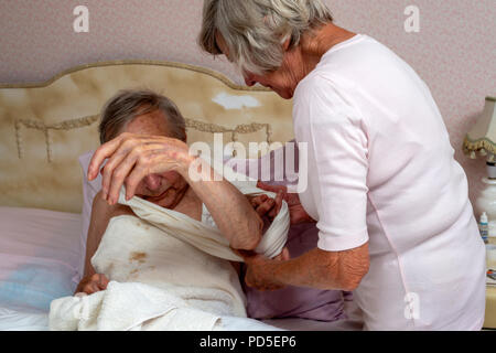 Elderly man being helped by his sister to get dressed Stock Photo