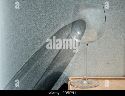 Broken wine glass with reflection from sunlight beam on wall plaster background Stock Photo