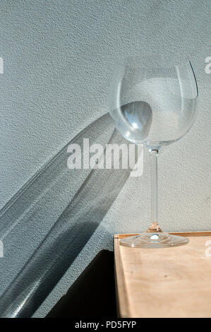 Broken wine glass with reflection from sunlight beam on wall plaster background Stock Photo