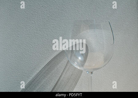 Broken wine glass with reflection from sunlight beam on wall plaster background Stock Photo