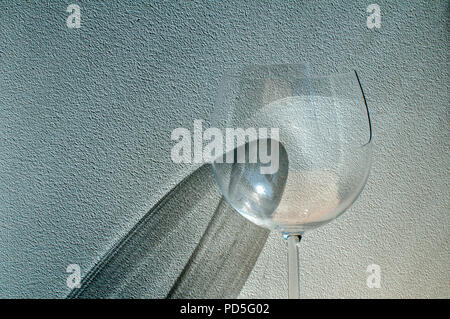 Broken wine glass with reflection from sunlight beam on wall plaster background Stock Photo
